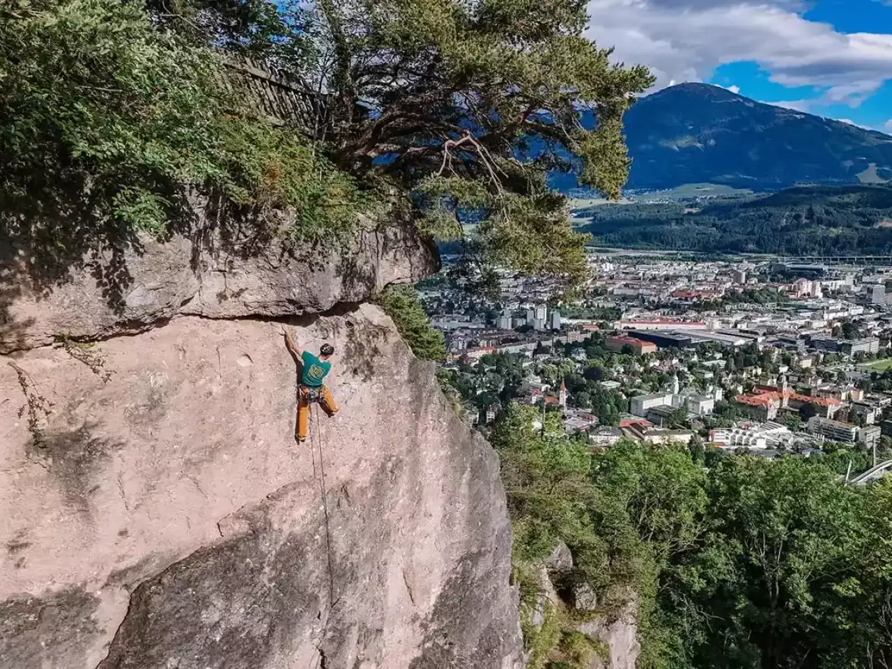 Mann klettert am Fels mit Innsbruck im Hintergrund